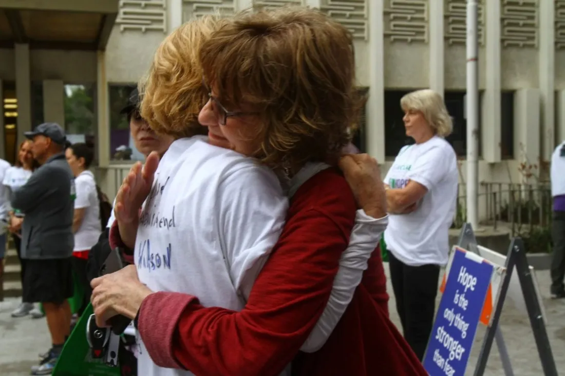 Two people embracing at an Our House Los Angeles community event, beside a sign that reads “Hope is the only thing stronger than fear”