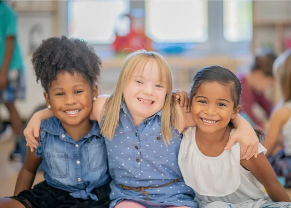 Three young children smiling with their arms around each other