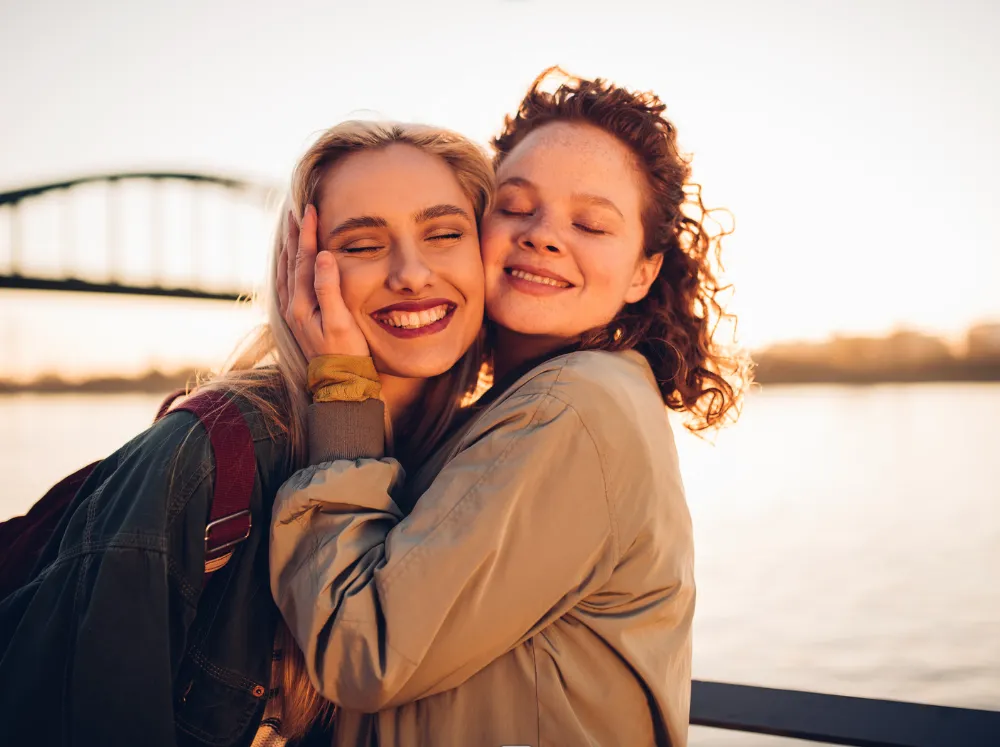 Two friends embracing and smiling at sunset